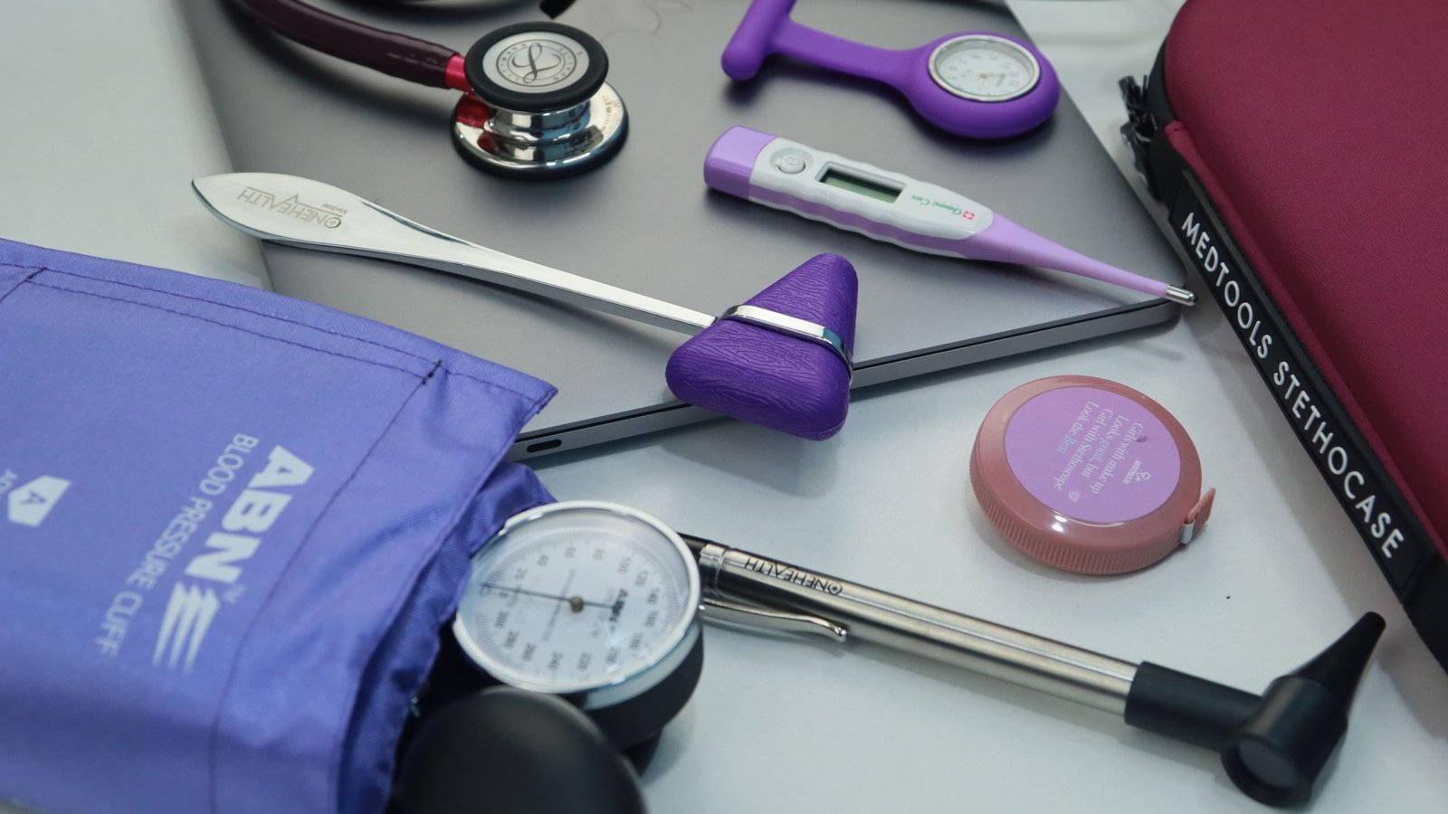Clinical tools laid out on a table: stethoscope, blood pressure cuff, reflex hammer and thermometer