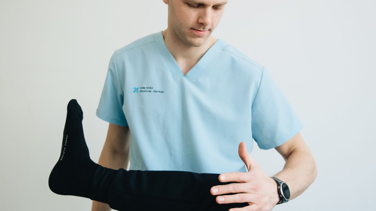 Physical therapist in blue scrubs moving a patient's leg through a hip and knee range-of-motion test