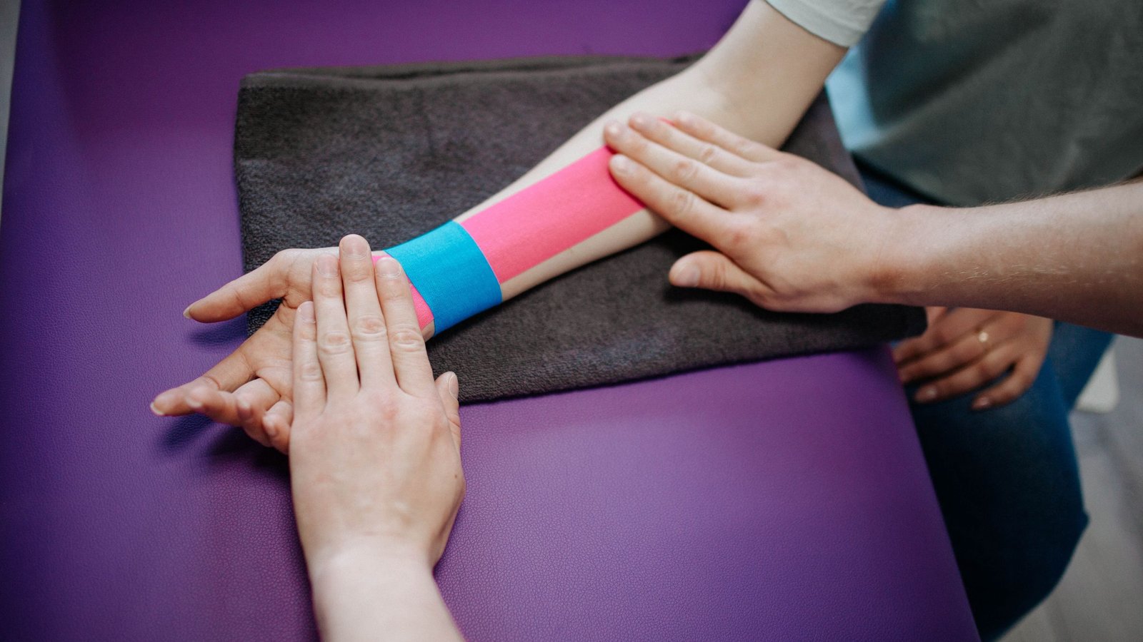 A clinician applies kinesiology tape to a patient's forearm